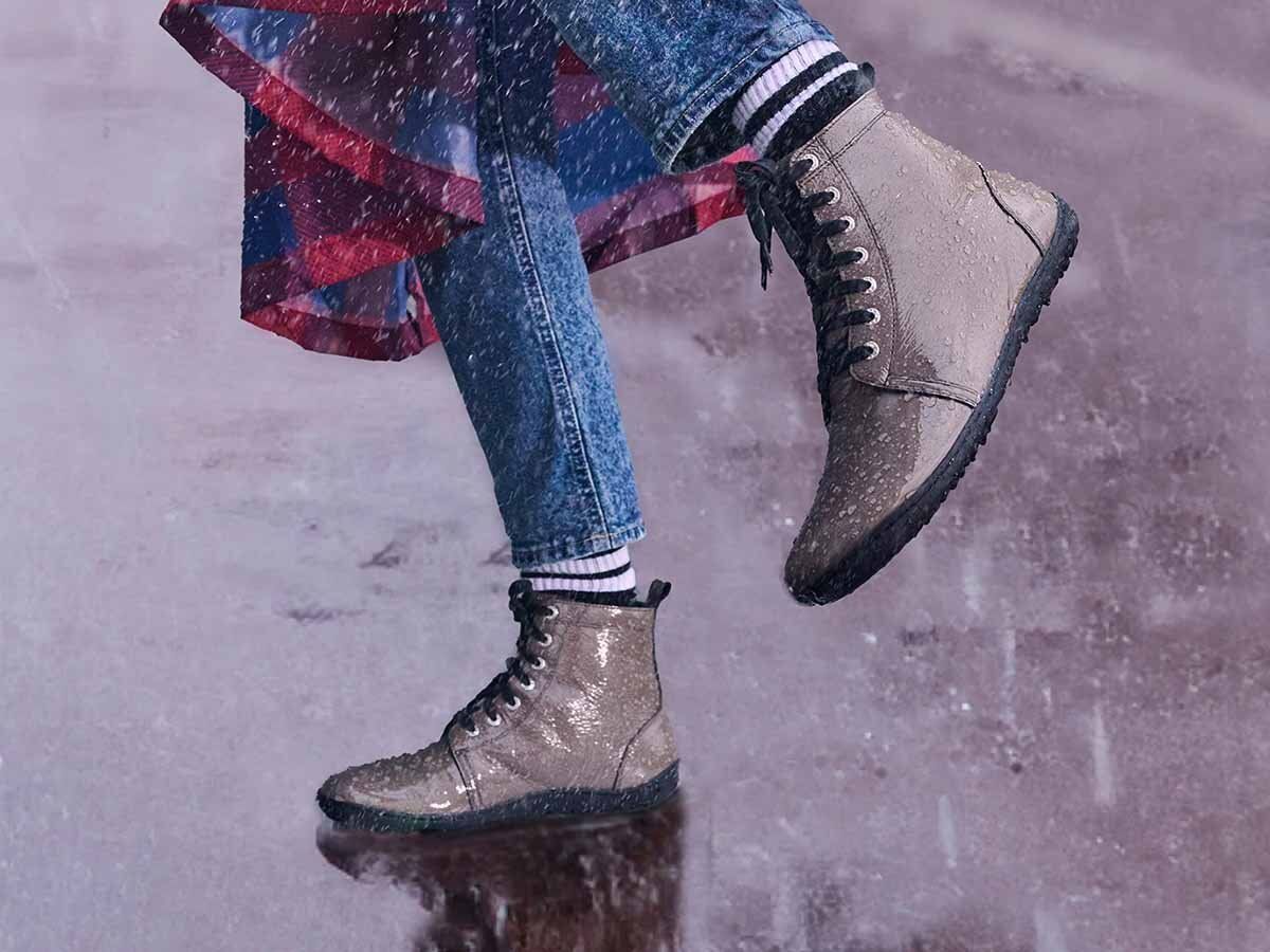 Person trägt braune Stiefeletten mit Schnürsenkeln. Glänzendes Obermaterial, schwarze Sohle. Im Regen.