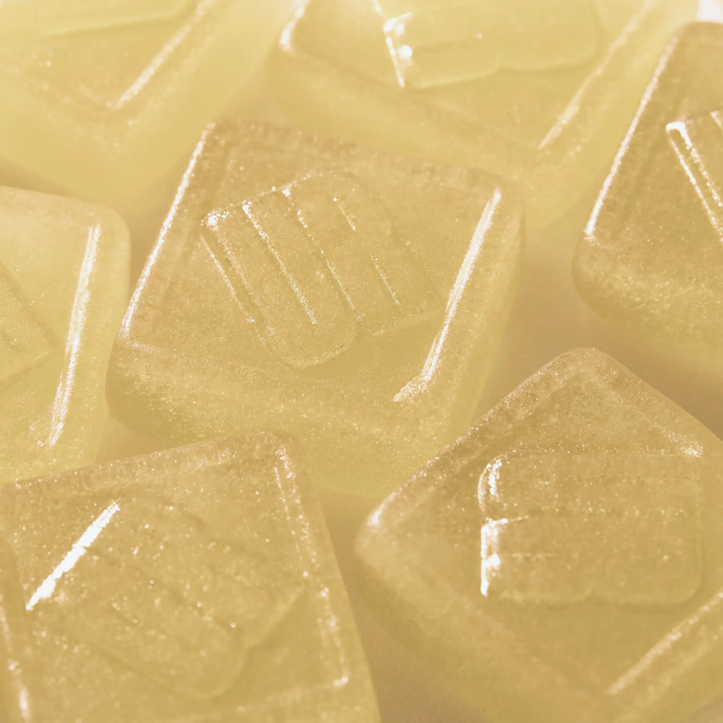 Mehrere gelbliche, quadratische Gummibärchen mit geprägtem Muster. Nahaufnahme, helle Beleuchtung.