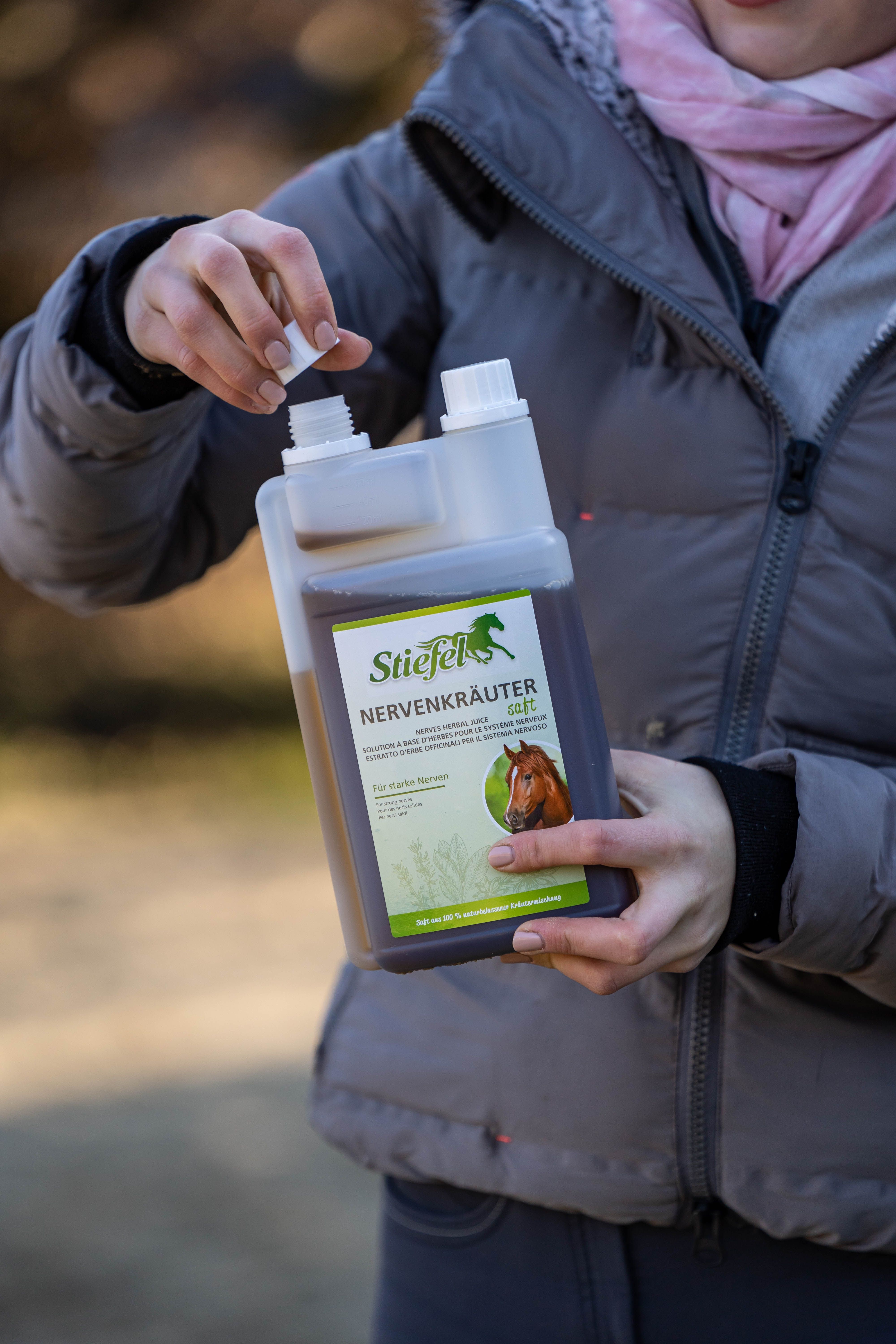 Person hält eine Flasche Stiefel Nervenkräutersaft. Die Flasche ist weiß und durchsichtig, mit einem grünen Etikett und einem Pferdekopf.