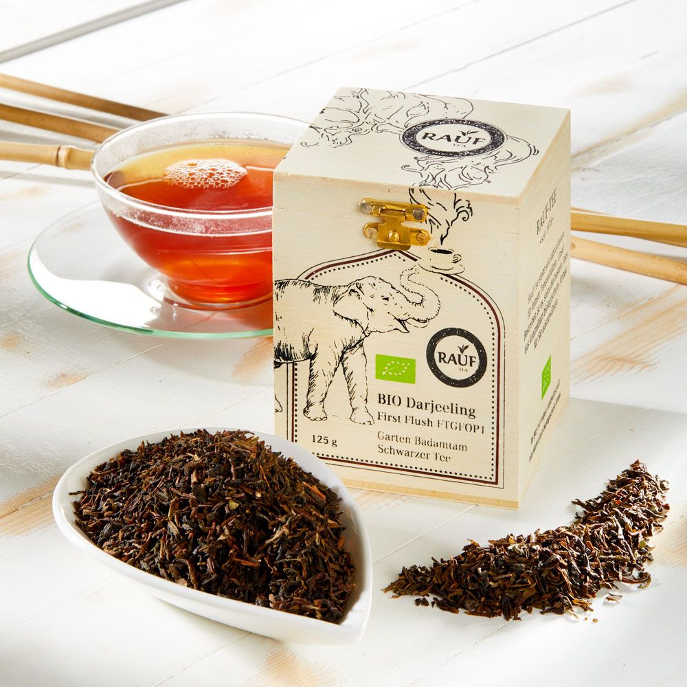 Holzkiste mit Aufdruck, Tasse Tee, lose Teeblätter. Aufschrift: Rauf, Bio Darjeeling, Schwarzer Tee.