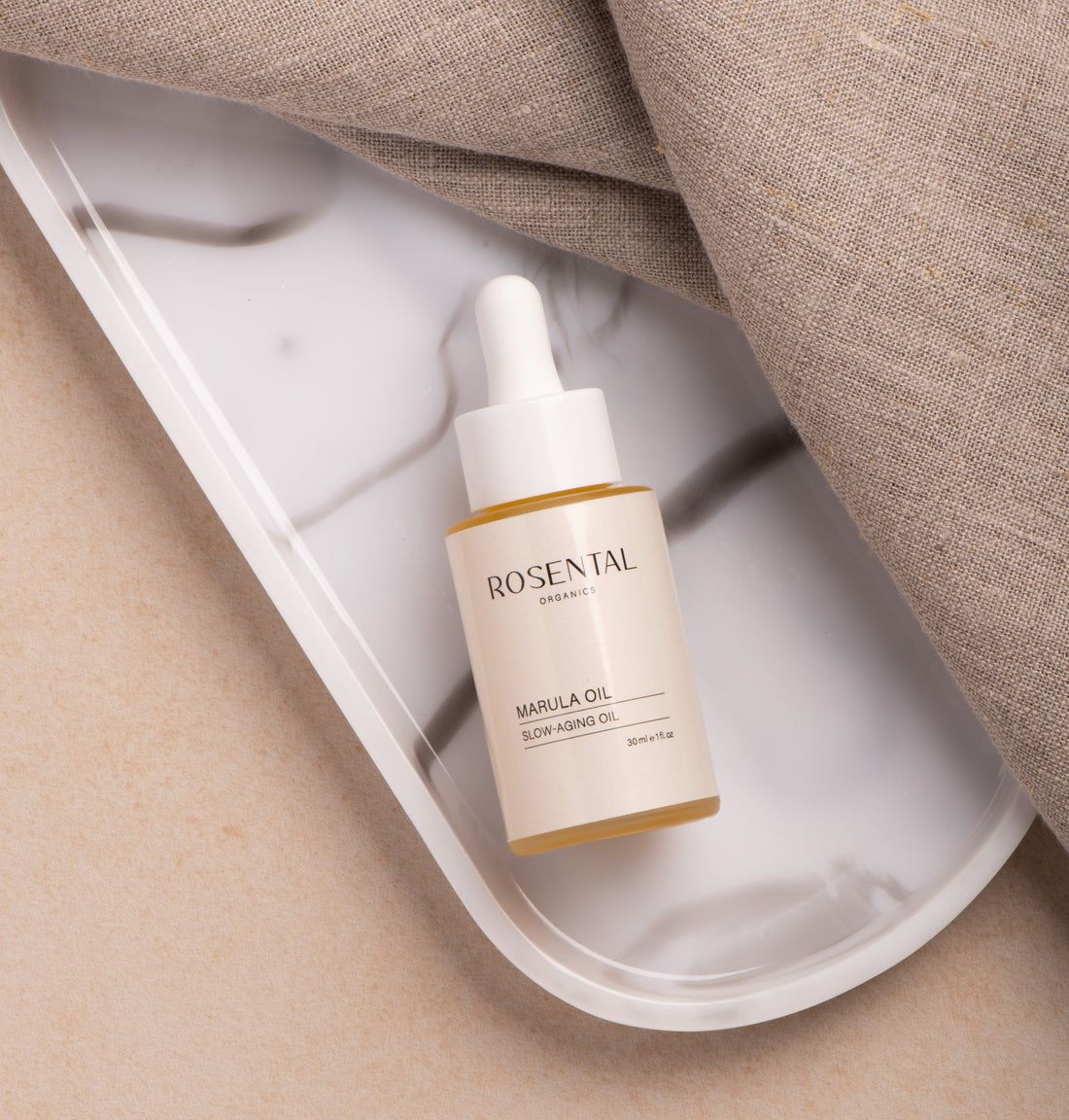 Rosental Organics Marula Oil Flasche auf einer weißen Marmorschale. Flasche mit weißem Deckel und beigem Etikett.