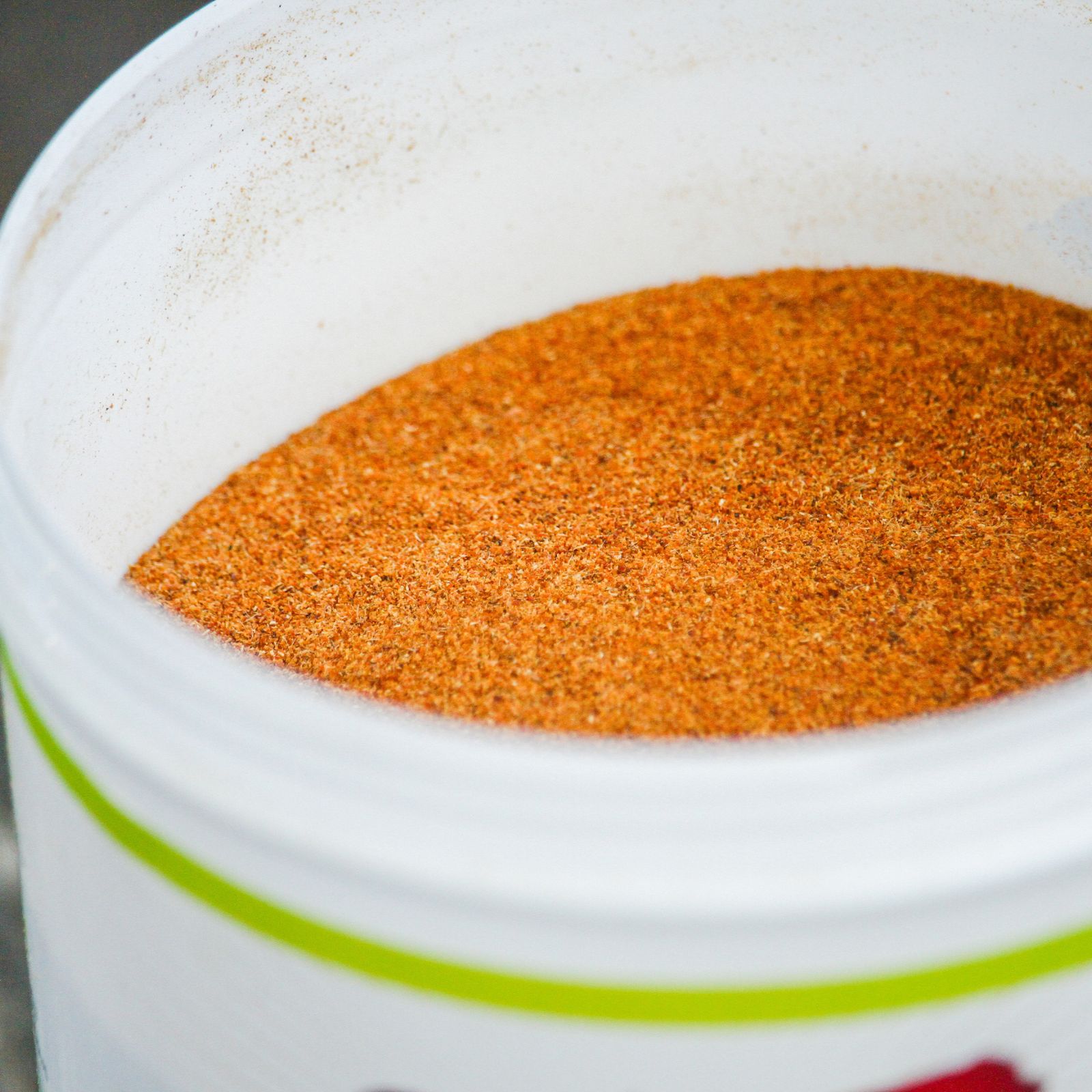 Nahaufnahme eines weißen Behälters mit orangefarbenem Pulver. Grüne Linie am Rand des Behälters sichtbar.