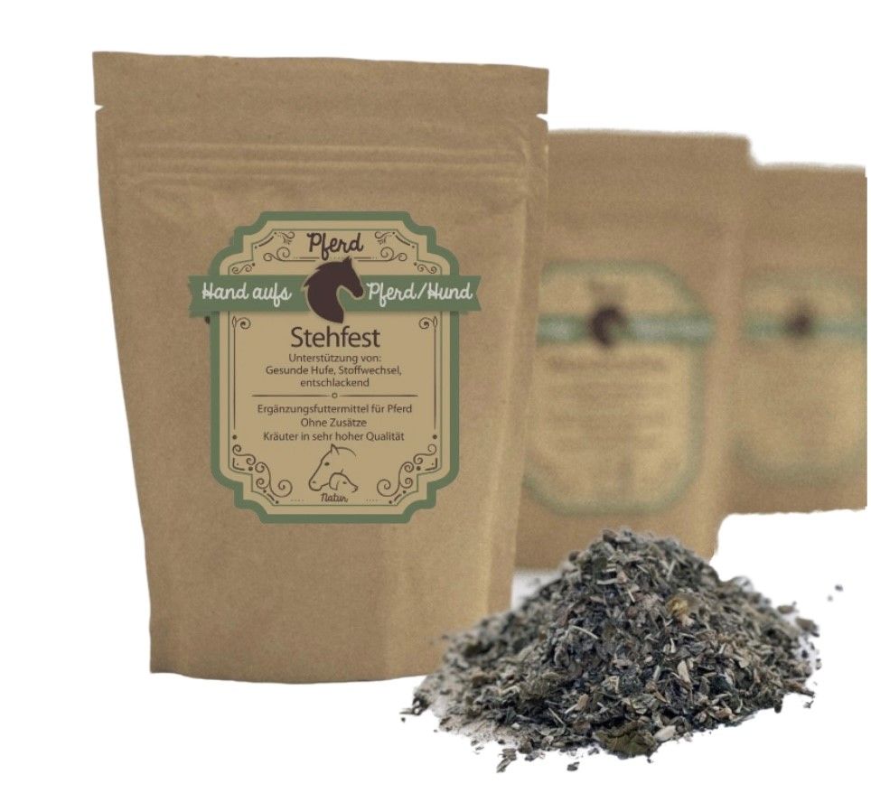 Beutel mit Kräutern. Aufschrift: Hand aufs Pferd/Hund, Stehfest. Braune Verpackung, grünes Etikett. Kräuterhaufen davor.