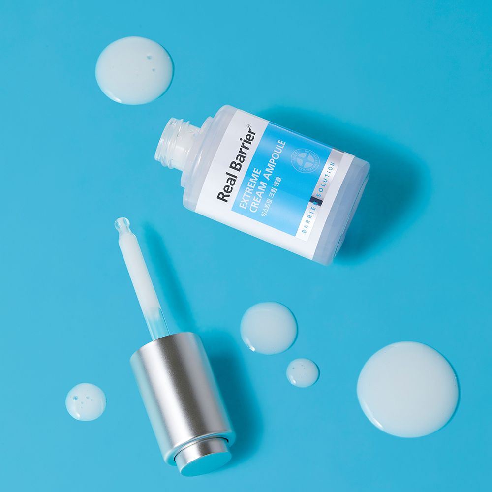 Serumflasche mit Pipette und Serumtropfen auf blauem Hintergrund. Aufschrift: Real Barrier Extreme Cream Ampoule.