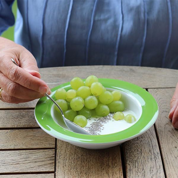 Grüne Schale mit Joghurt, Chiasamen und Weintrauben. Eine Hand hält eine Löffel.