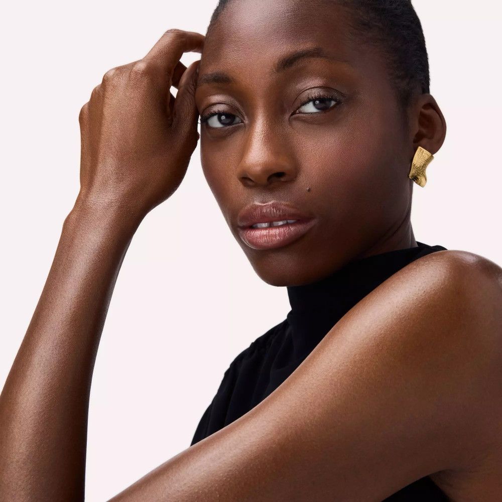 Dunkelhäutige Frau. Trägt goldene Ohrringe. Blick in die Kamera. Schwarzes Oberteil.