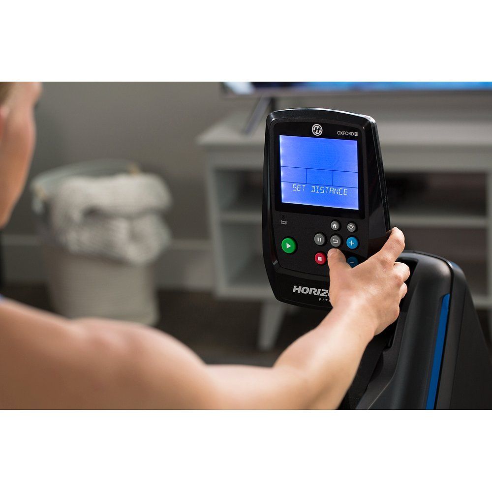 Person hält Bedienfeld eines Rudergeräts. LCD-Anzeige mit Text. Horizon Fitness Logo.