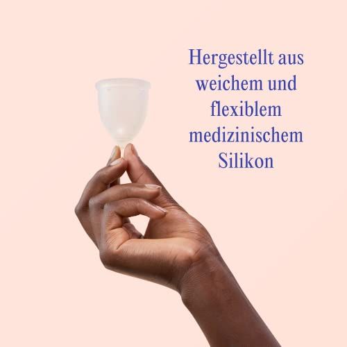 Hand hält eine transparente Menstruationstasse aus weichem, flexiblem medizinischem Silikon. Rosa Hintergrund.