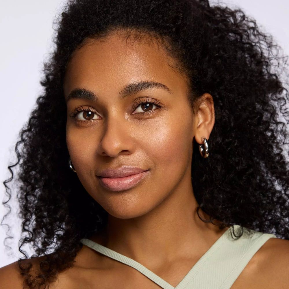 Porträt einer Frau mit lockigem Haar. Sie trägt einen grünen Top und Ohrringe.