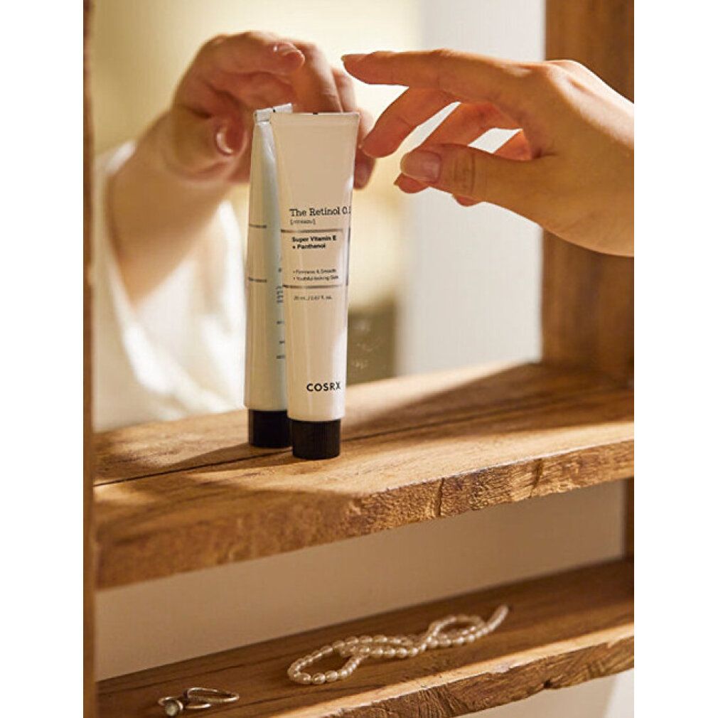 Eine Hand greift nach einer Tube 'The Retinol 0.1 Cream' von COSRX, die auf einem Holzregal steht.