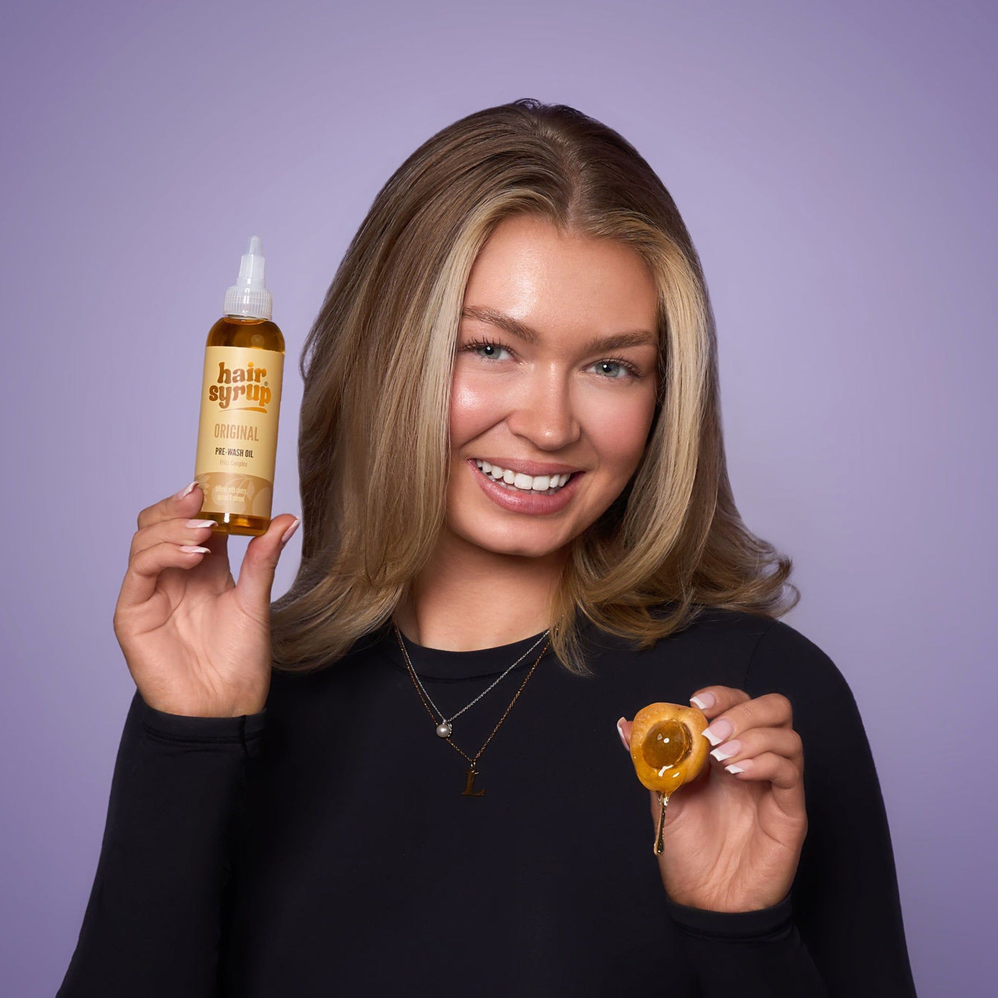 Frau hält eine Flasche Hair Syrup The Original und eine Frucht. Sie lächelt in die Kamera.