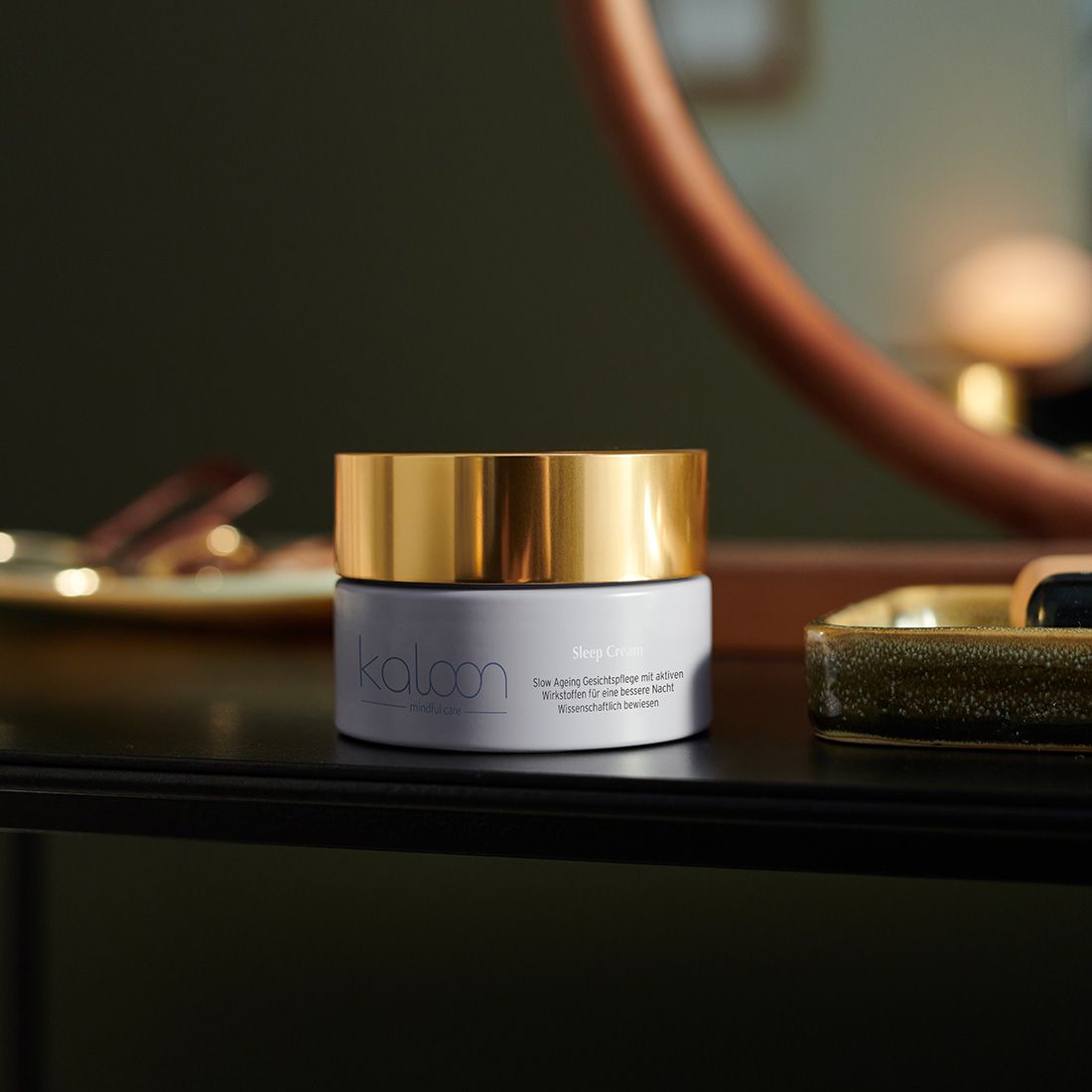 Creme-Tiegel mit goldfarbenem Deckel auf einer schwarzen Oberfläche. Auf dem Etikett steht "kaloon" und "Mindful Care".