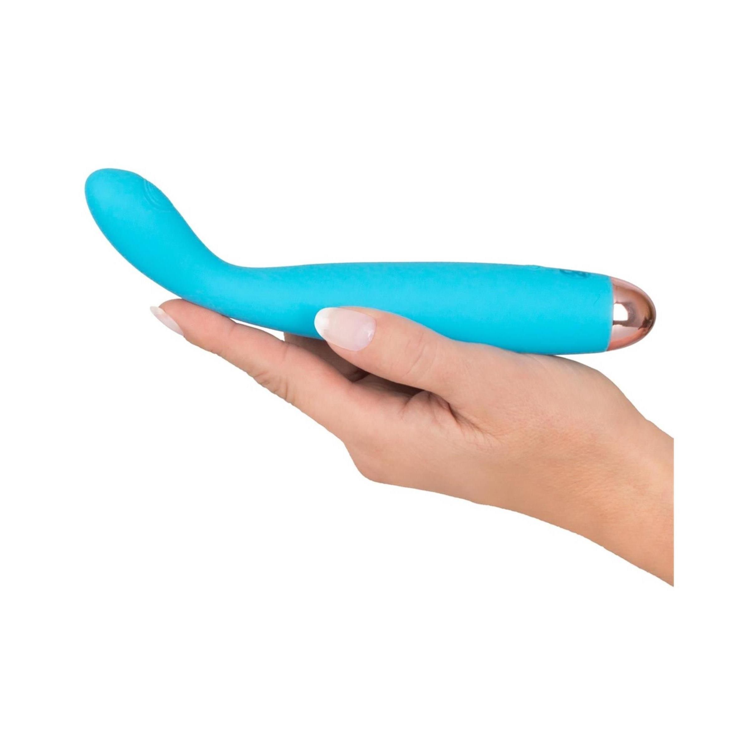 Hand hält türkisfarbenen Vibrator mit goldfarbener Spitze. Auf weißem Hintergrund.