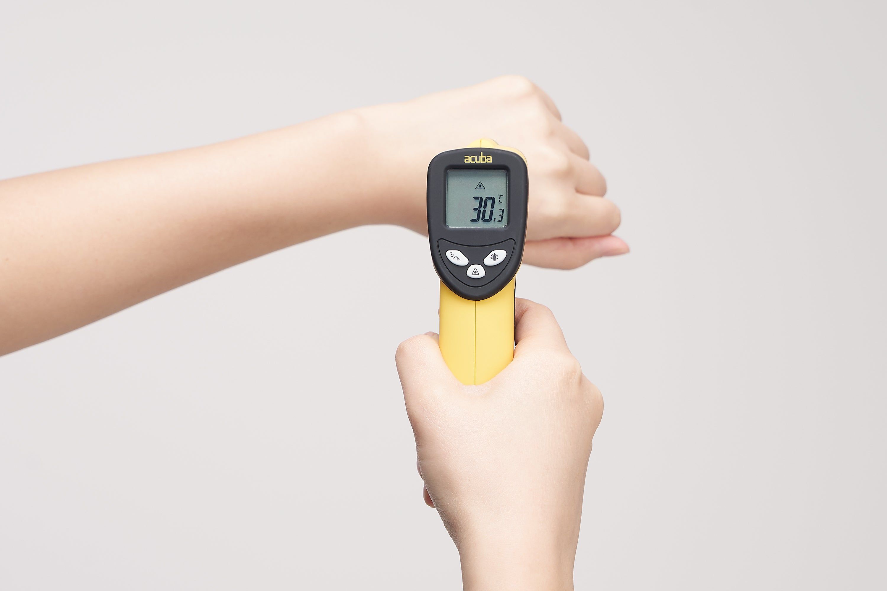 Hand hält ein gelbes Thermometer an einem Arm. Anzeige: 30.1. Auf weißem Hintergrund.