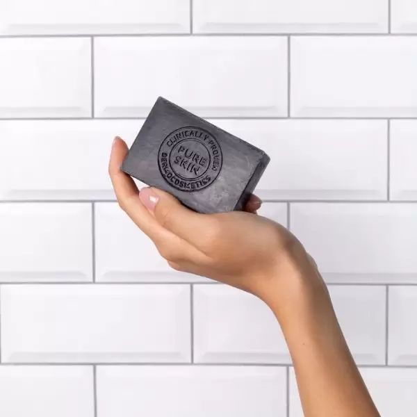 Schwarze Seife in Hand. Aufschrift: Pure Skin, klinisch getestet. Rechteckige Form. Seife wird von einer Hand gehalten, vor weißem Hintergrund.
