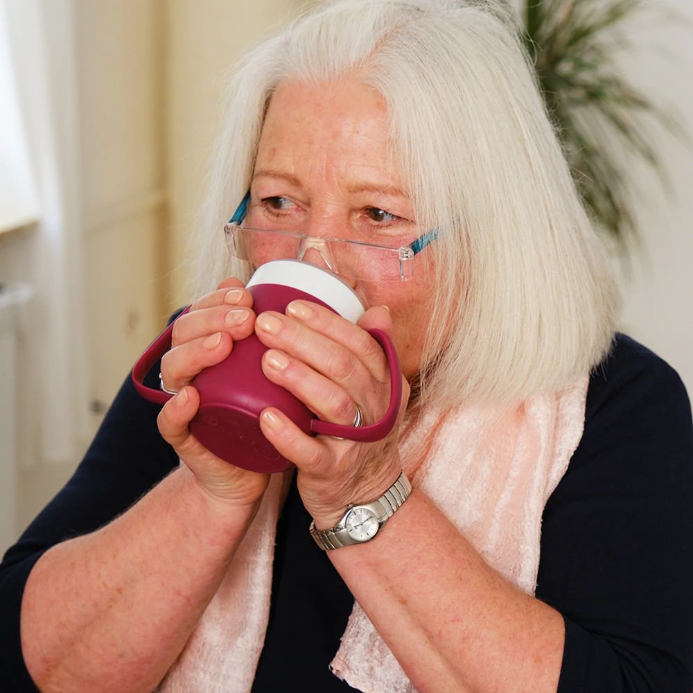 Person trinkt aus einem Becher mit Trink-Trick. Becher mit zwei Henkeln, rot.