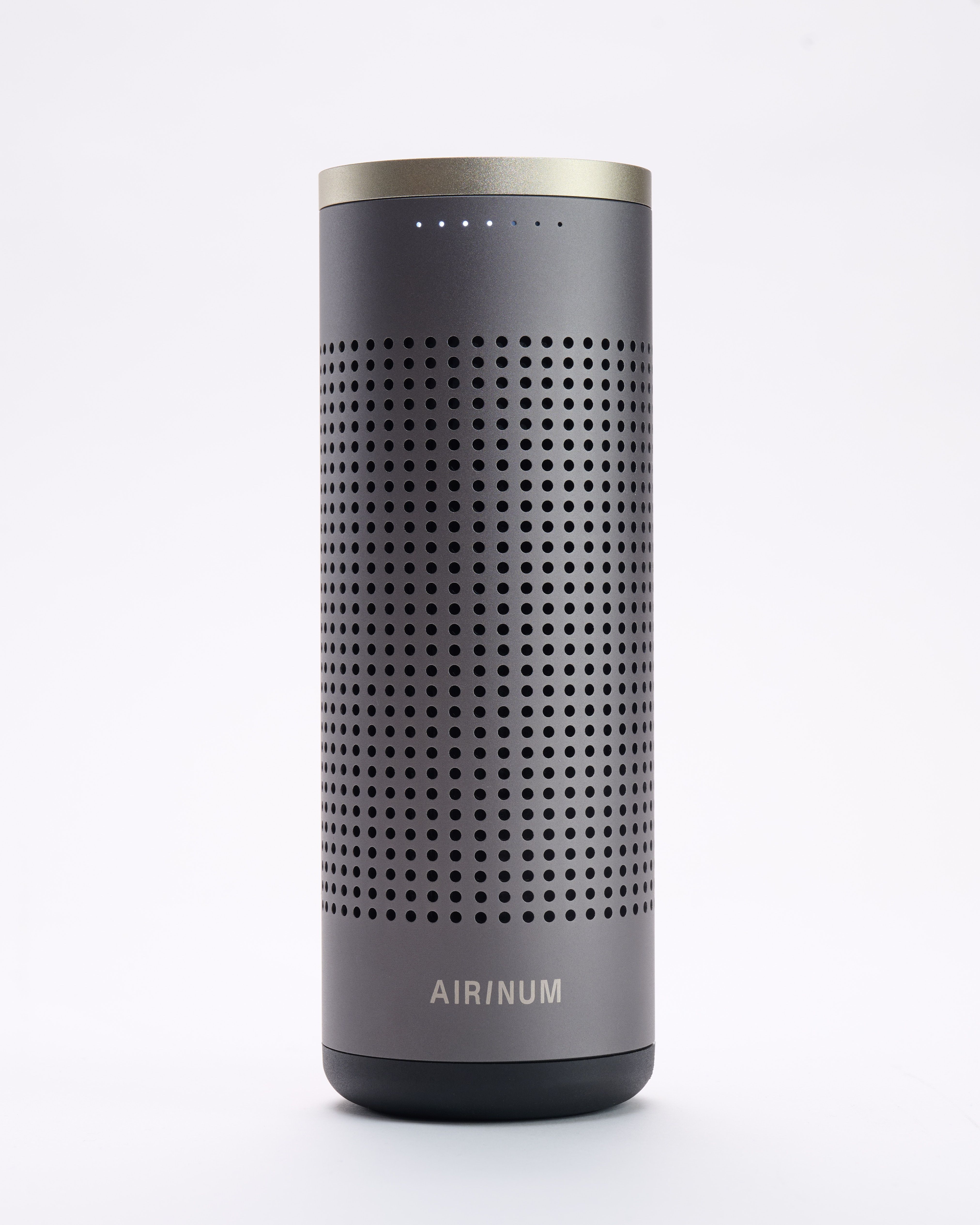 Graues zylindrisches Gerät mit perforierter Oberfläche. AIRINUM-Logo unten. Oberseite mit silbernem Ring.