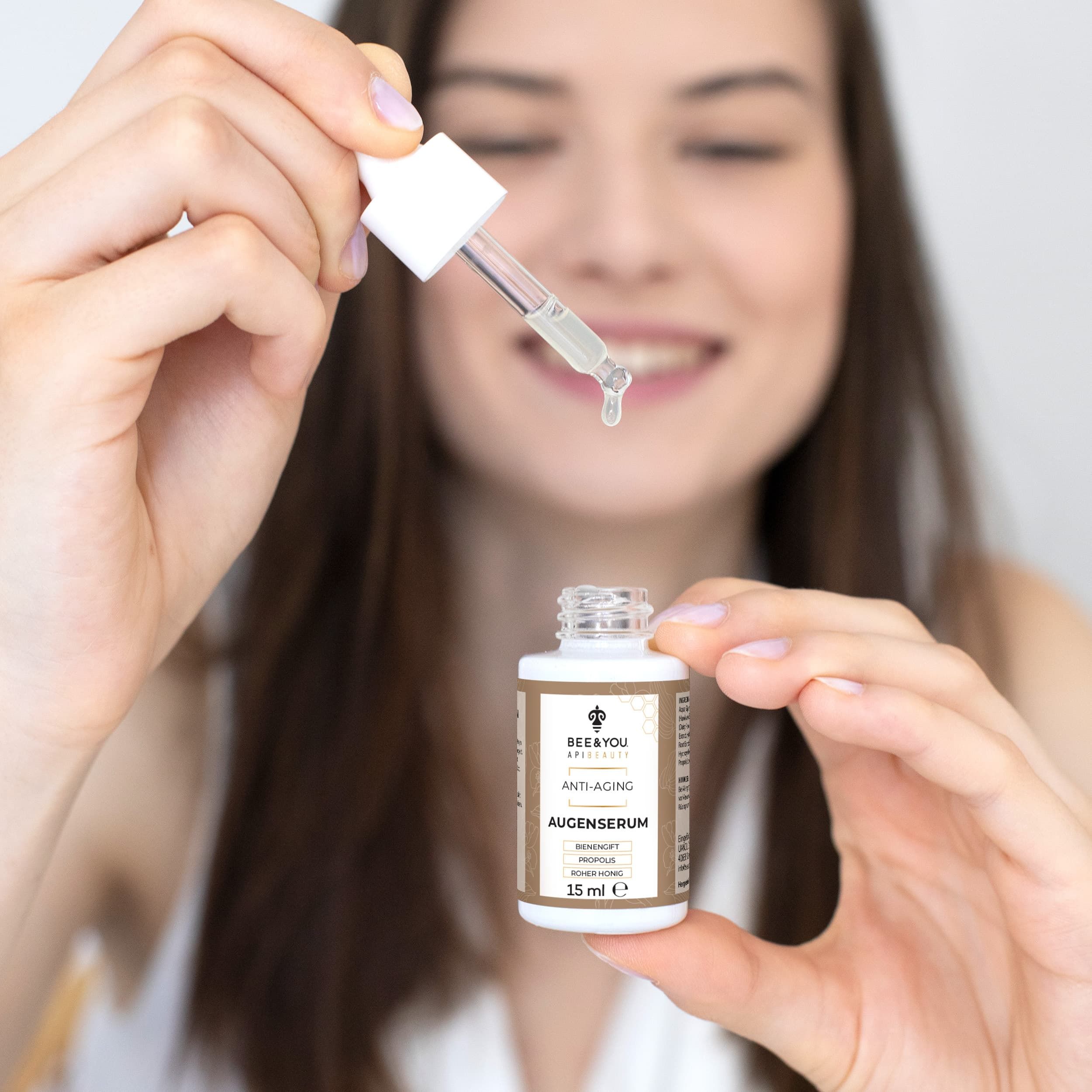 Frau hält eine kleine Flasche Augenserum und eine Pipette. Die Pipette tropft. Auf der Flasche steht Anti-Aging.