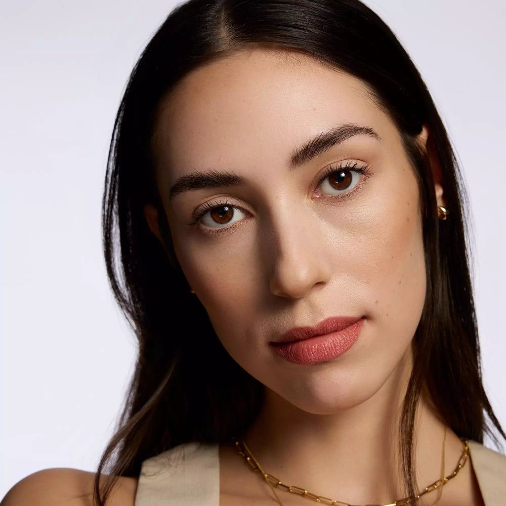 Nahaufnahme eines Gesichts mit Lippen, die mit Catrice Creamy Nudes Lippenkonturenstift geschminkt sind. Frau mit goldener Halskette.