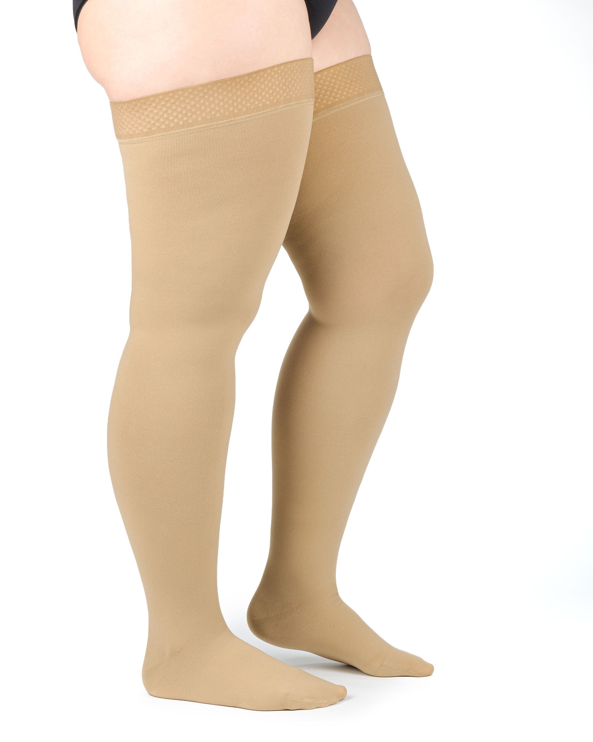 Beige Kompressions-Schenkelstrümpfe. Feines Netzmuster am Haftband. Blick von der Seite auf die Beine.