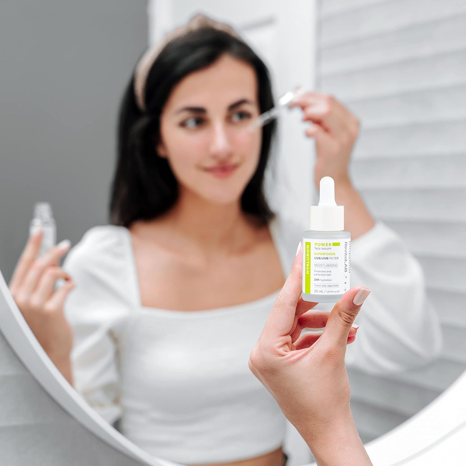 Frau hält Serumflasche vor Spiegel. Flasche mit Pipette. Produktinformationen sichtbar.