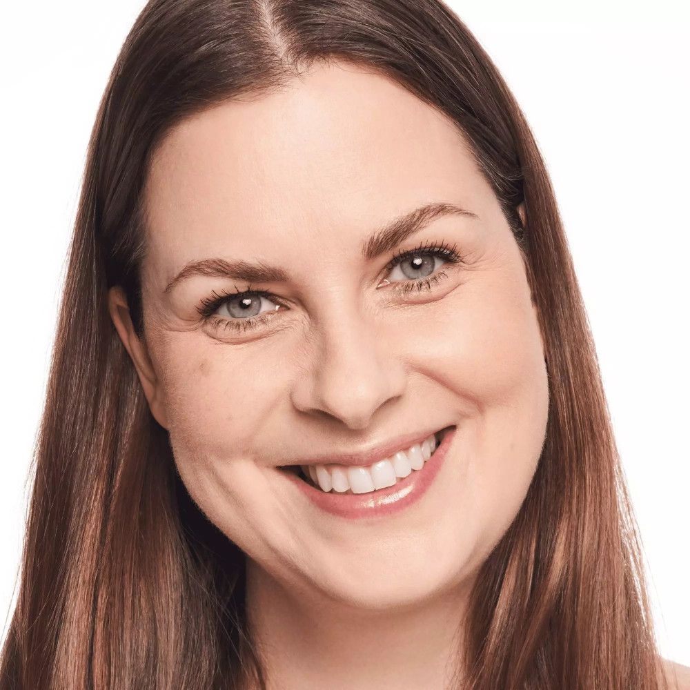 Porträt einer Frau mit braunen Haaren. Sie lächelt. Heller Hintergrund.