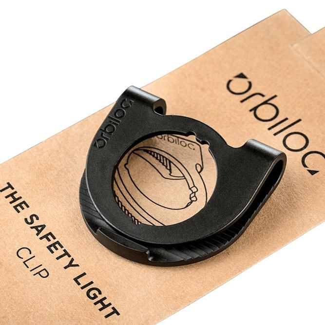 Schwarzer Clip für Sicherheitslicht. Auf brauner Verpackung mit "Orbiloc" und "The Safety Light Clip" beschriftet.