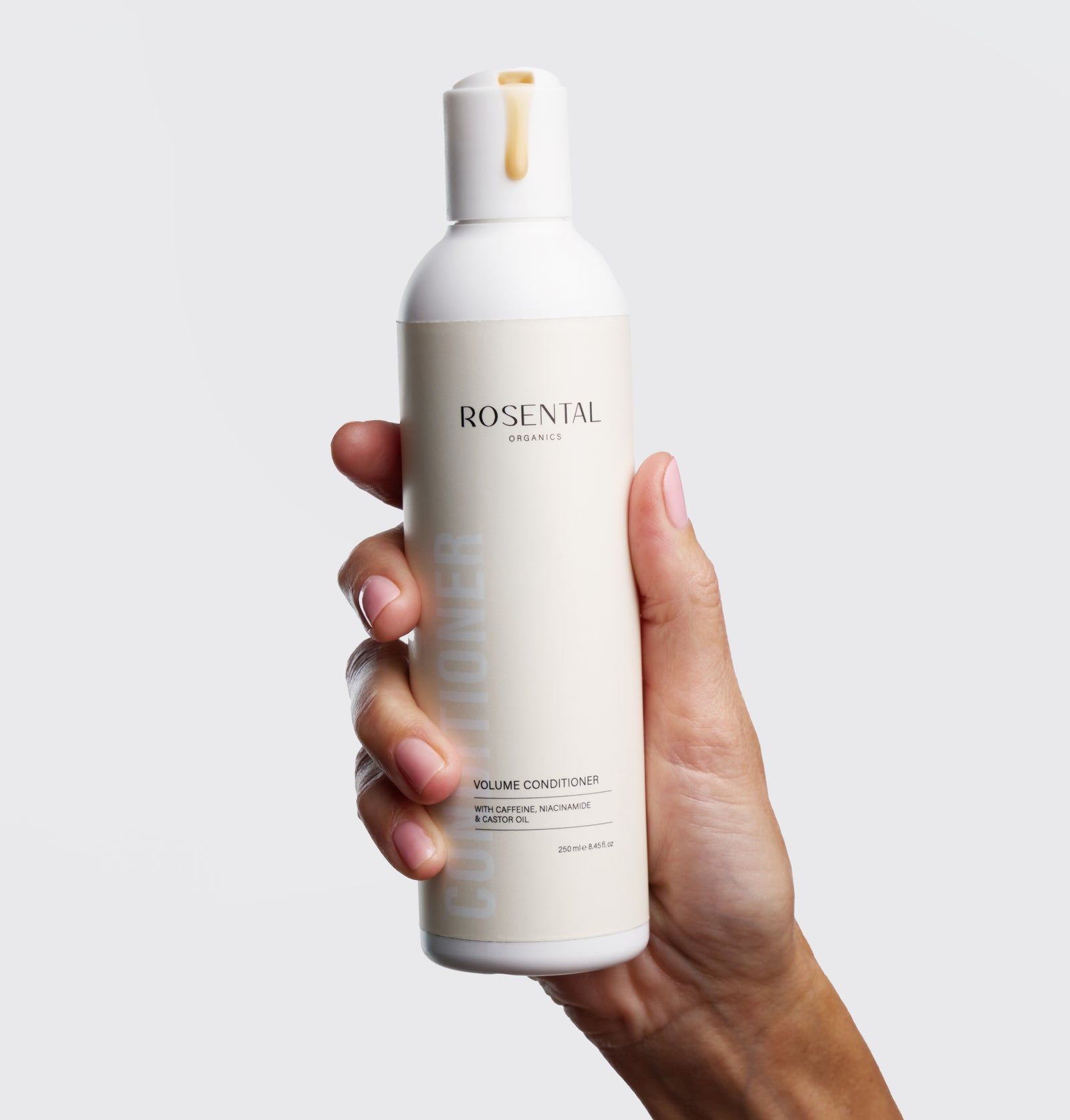 Eine Hand hält eine weiße Flasche Rosental Organics Volume Conditioner. Aufschrift: Volume Conditioner. Hintergrund: weiß.