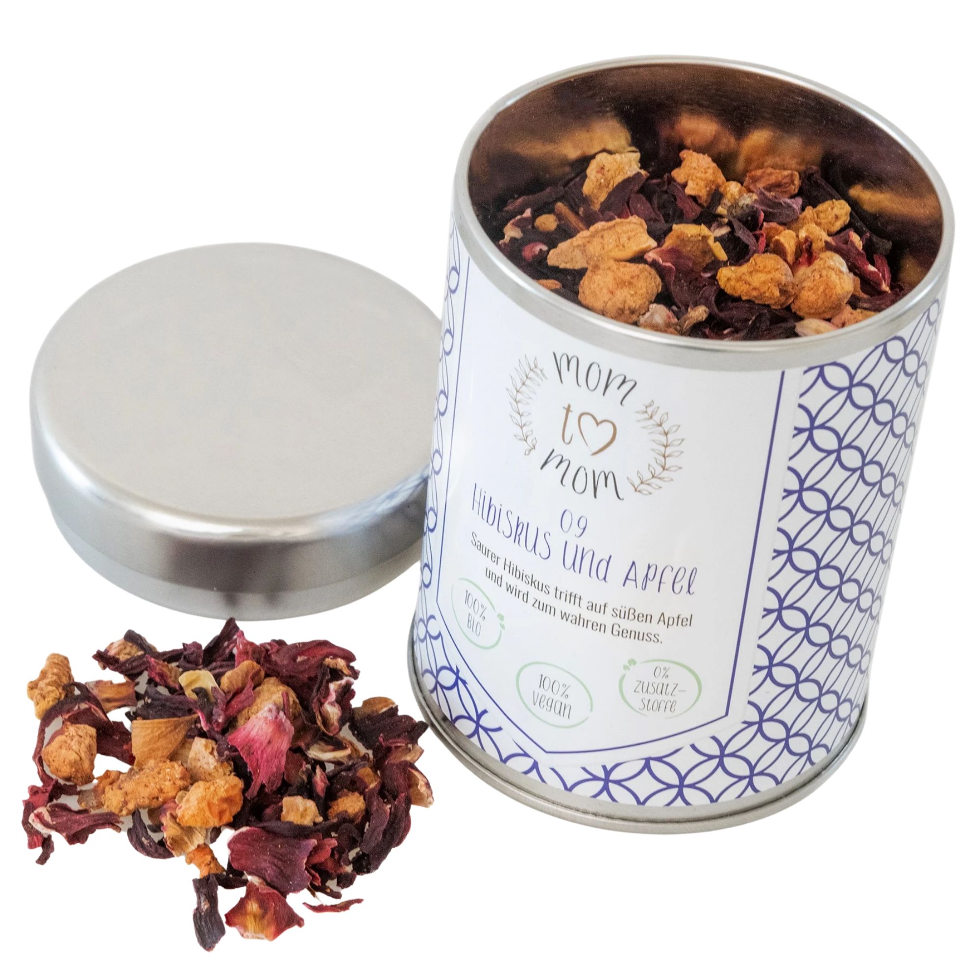Geöffnete Teedose mit losem Tee, daneben Deckel und Tee. Dose mit Aufschrift 'mom to mom' und 'Hibiskus & Apfel'.