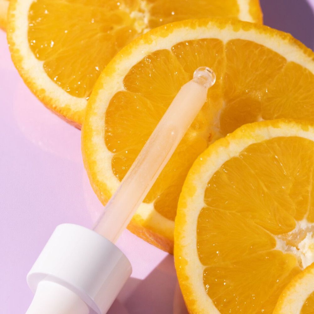 Pipette mit Serumtropfen und Orangen. Transparente Flüssigkeit.