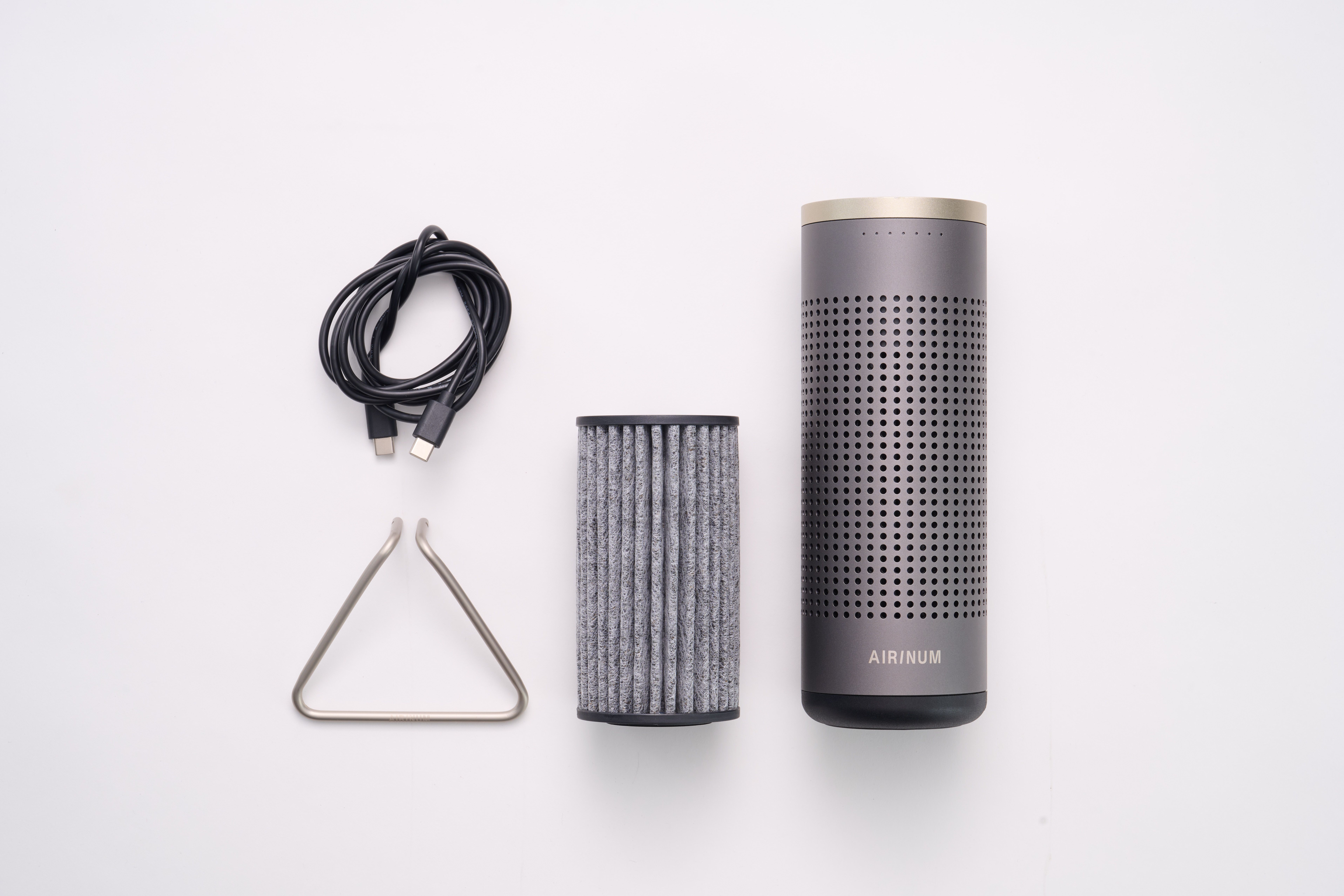 Gerät, Filter, Metallständer und Kabel. Gerät grau, zylindrisch mit perforierter Oberfläche. AIRINUM-Logo.