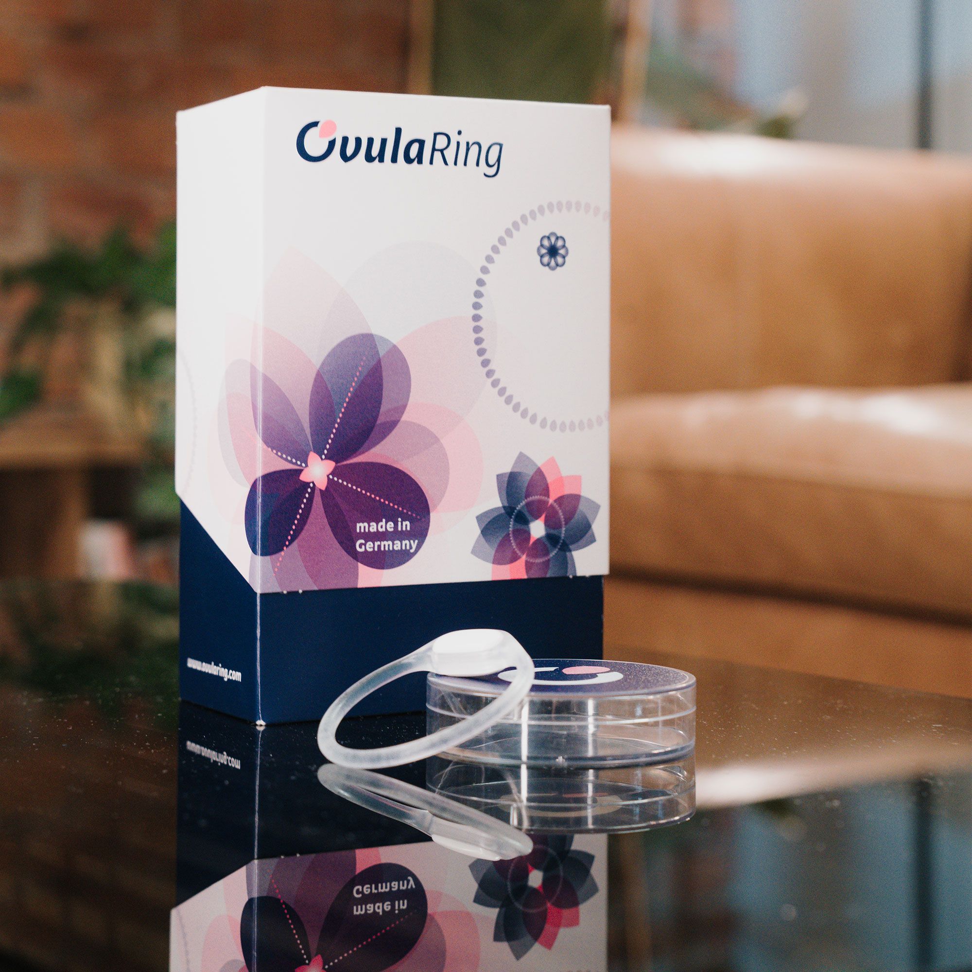 OvulaRing-Verpackung und Ring auf Tisch. Verpackung weiß-rosa, Ring transparent. Aufschrift OvulaRing.