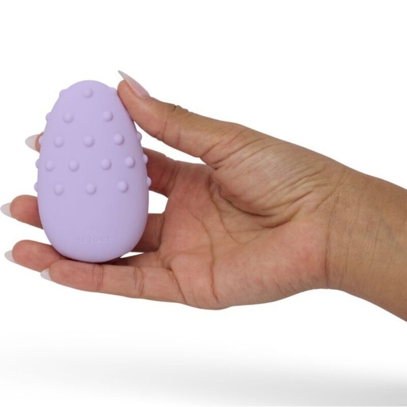Lila Massagegerät in einer Hand gehalten. Ei-Form mit Noppen. Marke Je Joue.