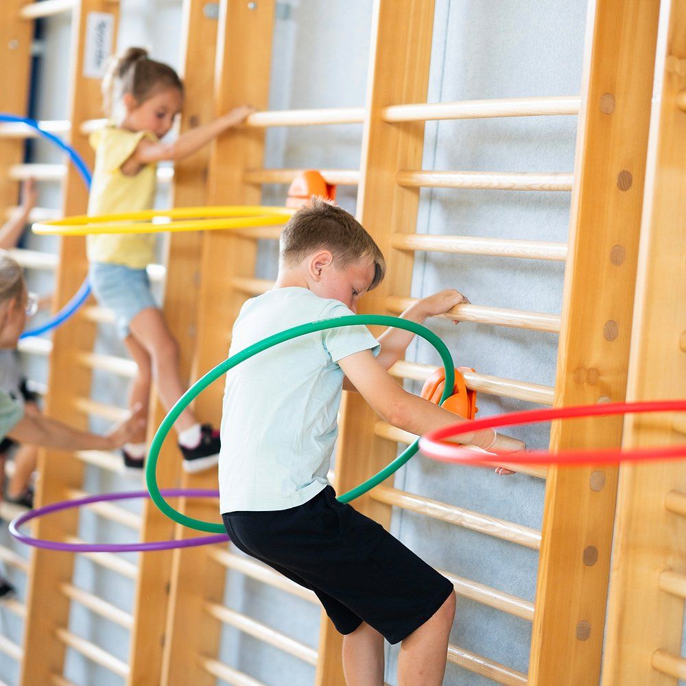 Kinder klettern an Sprossenwand mit Reifenhaltern und Reifen. Mehrere Reifen in verschiedenen Farben.