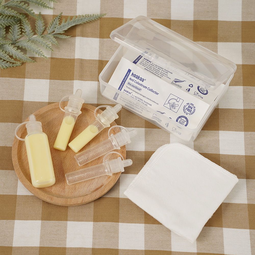 Set aus Behältern mit gelblicher Flüssigkeit, Tüchern und einer Aufbewahrungsbox auf einem Holzbrett. Auf der Box steht "Haakaa".