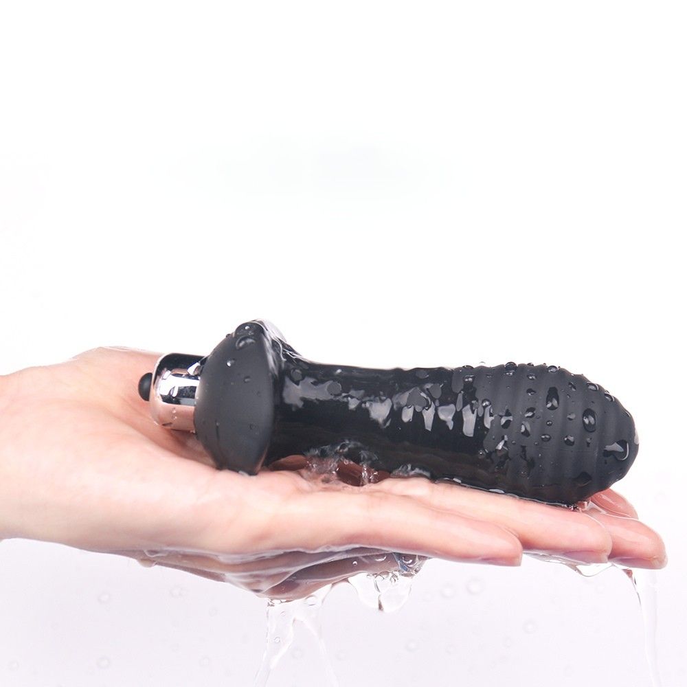 Schwarzer Analvibrator in einer Hand, nass. Wasser fließt.