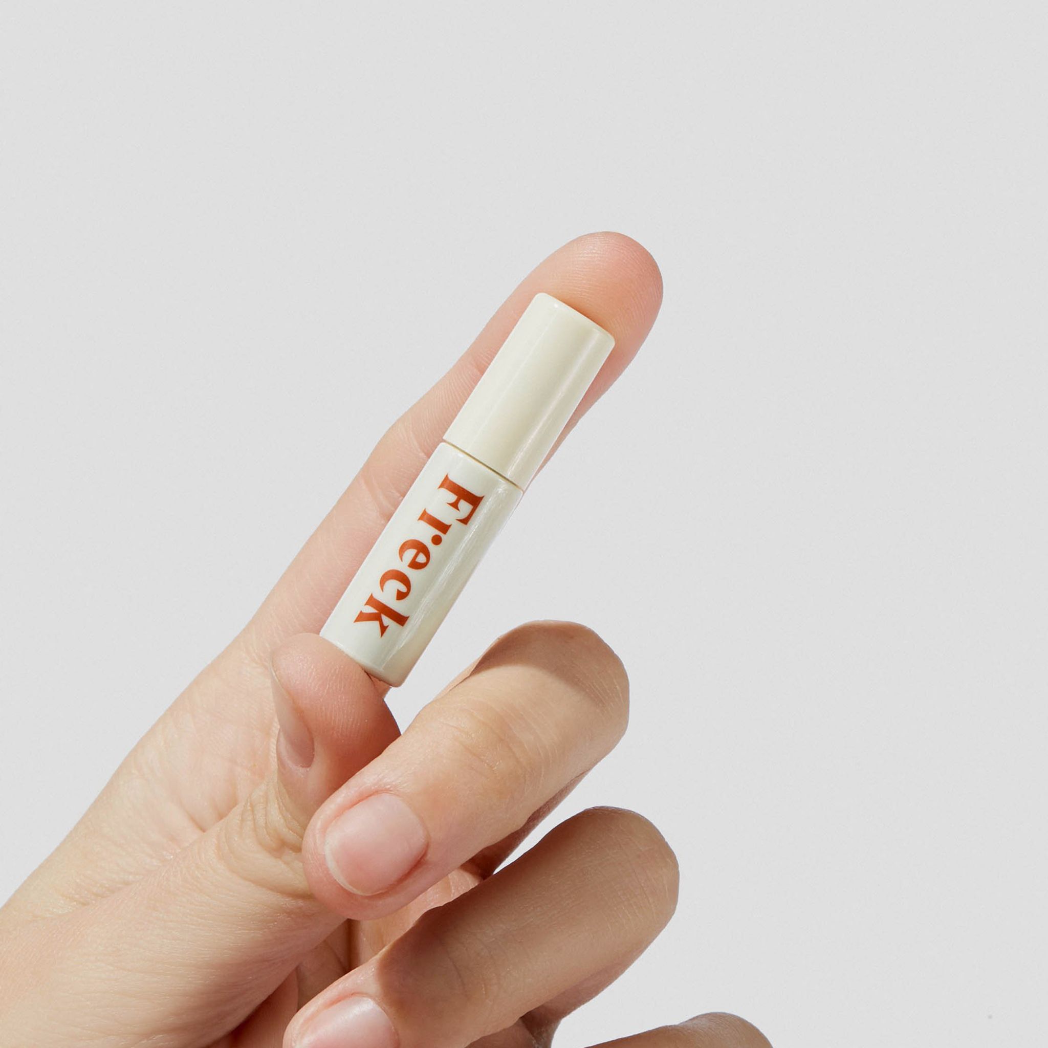 Tubo con scritta "Freck" rossa, tenuto da una mano. Tappo bianco.