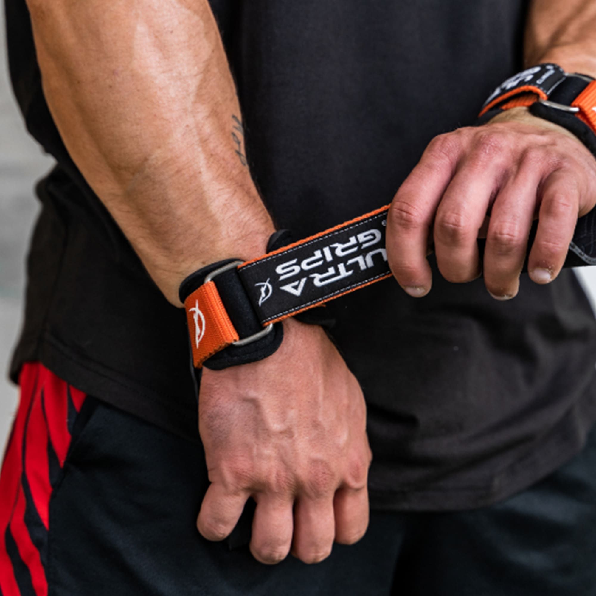Person trägt Ultra-Grips. Schwarzes Band mit "ULTRA GRIPS" und orangefarbenen Akzenten.