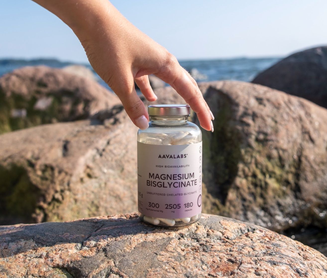 Hand hält Flasche mit Kapseln auf Felsen. Aufschrift: Magnesiumbisglycinat.