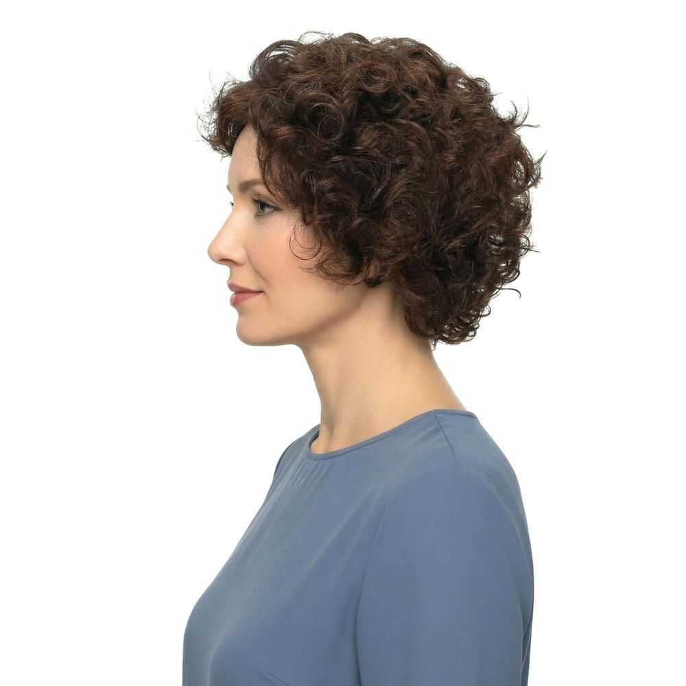 Frau mit brauner, lockiger Perücke. Seitenansicht. Sie trägt ein blaues Oberteil. Hintergrund weiß.