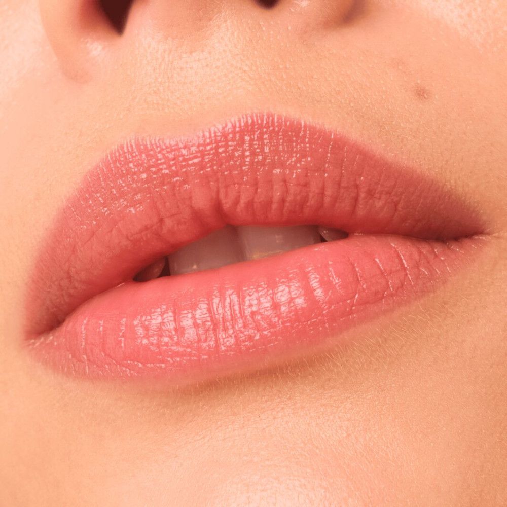 Nahaufnahme von Lippen, die mit einem glänzenden, rosafarbenen Produkt bedeckt sind.