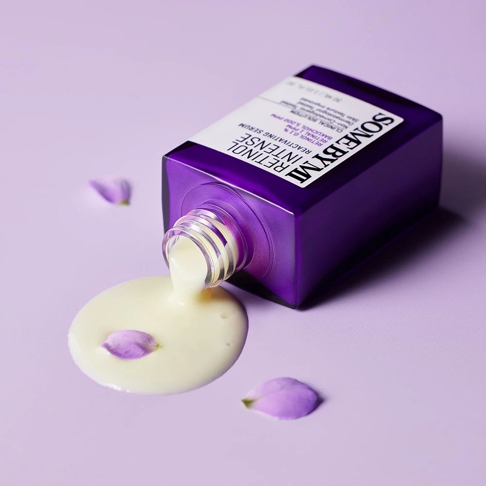Violette Flasche mit Serum, Serum fließt heraus. Produktname und Text sind sichtbar.