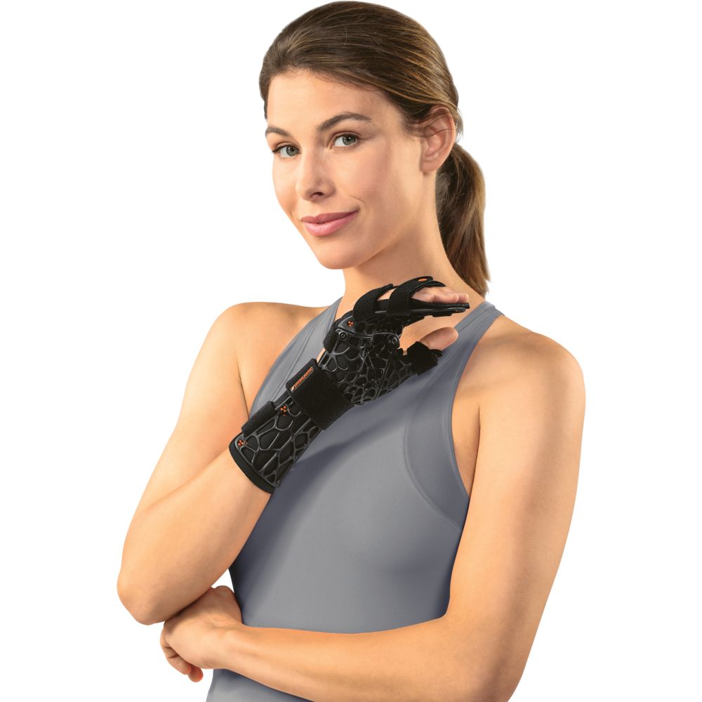 Frau mit Handgelenkorthese. Schwarze Orthese am linken Arm. Graues Top. Blick in die Kamera.