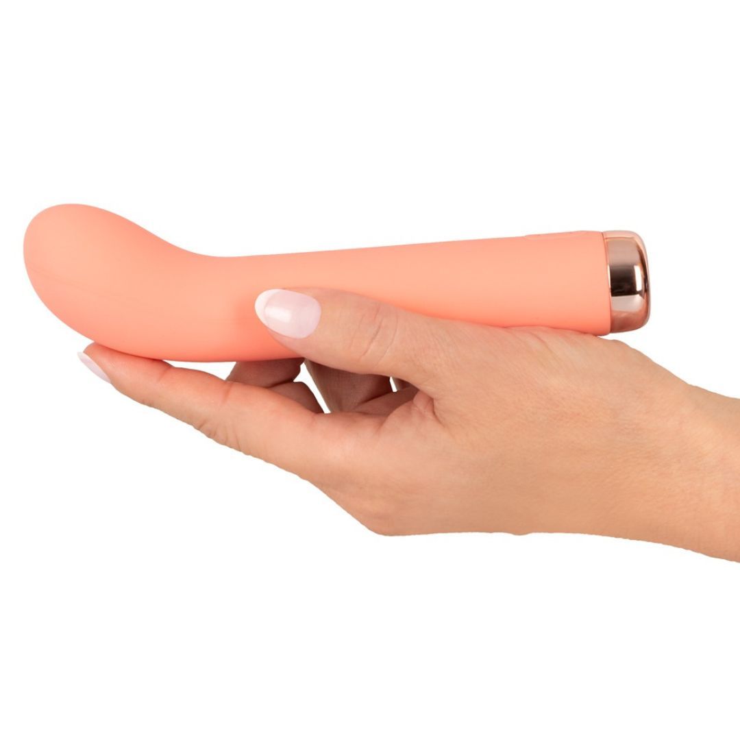 Korallenfarbener Vibrator in einer Hand gehalten. Goldfarbener Sockel. Glatte Oberfläche.