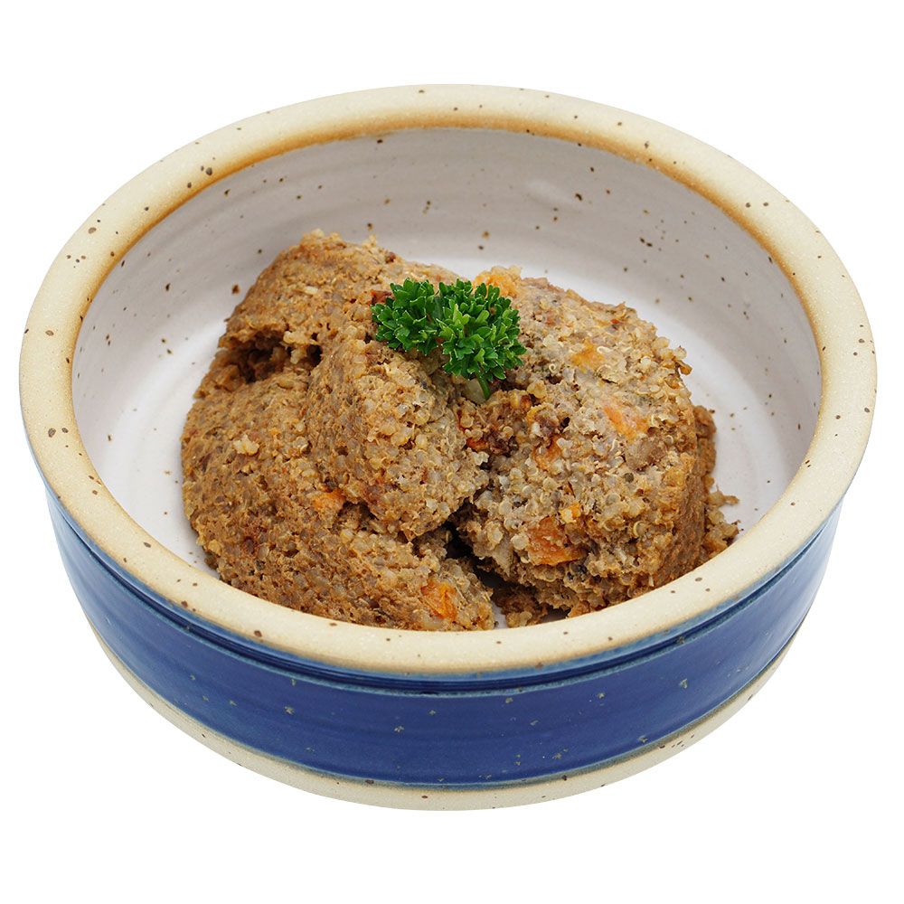 Hundefutter in einer Keramikschale. Das Futter ist braun und enthält Gemüse. Ein grünes Kraut garniert das Futter.