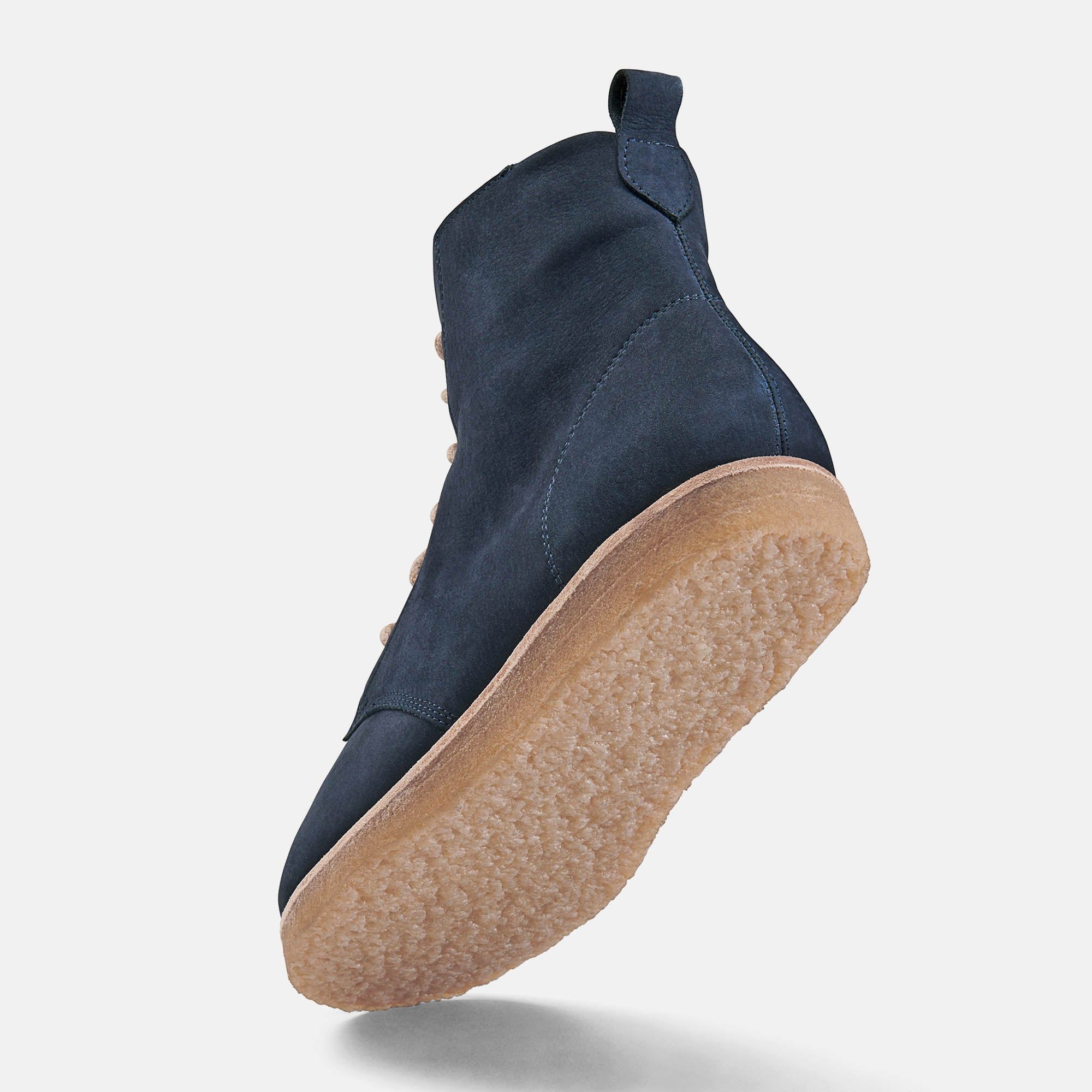 Blaue Stiefelette von hinten. Beige Sohle. Hellgrauer Hintergrund. Schuh schwebt.