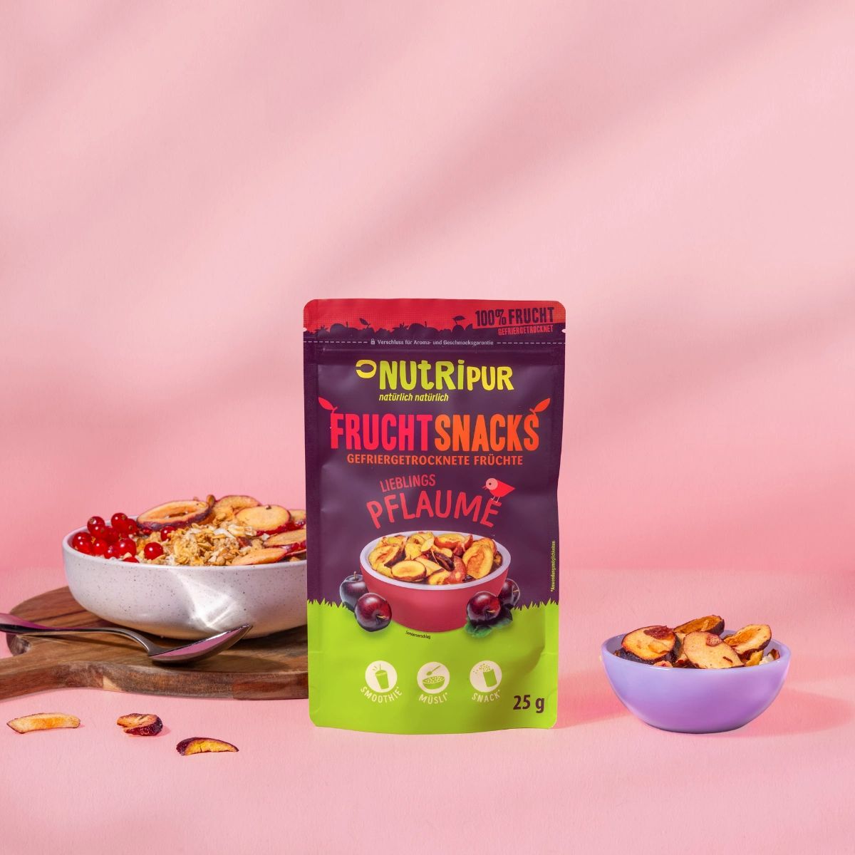 Beutel mit gefriergetrockneten Pflaumen-Snacks. Auf Holzbrett mit Schüssel Müsli, Beeren und Pflaumen. Kleine Schüssel mit Pflaumen.