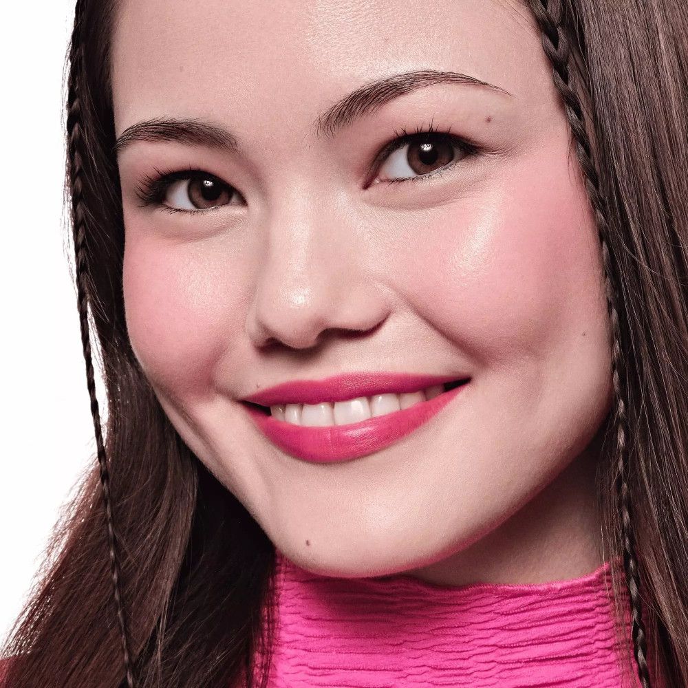 Nahaufnahme eines Gesichts. Gebräunte Haut mit rosa Wangen und Lippen. Dunkle Haare mit Zöpfen.