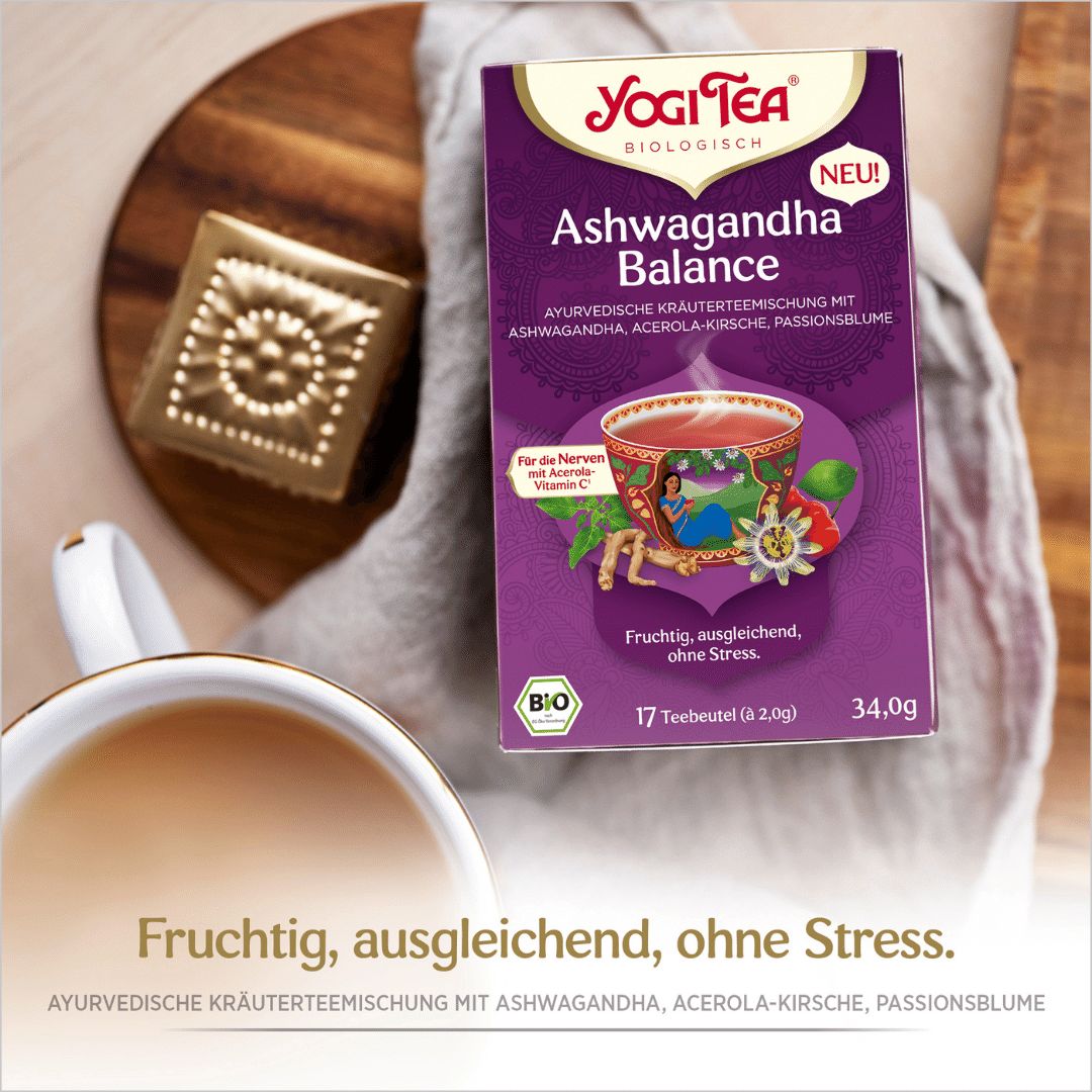 Yogi Tea Ashwagandha Balance Packung auf Holz. Lila Verpackung mit Logo, Produktname und Inhaltsangaben. Bio-Siegel.