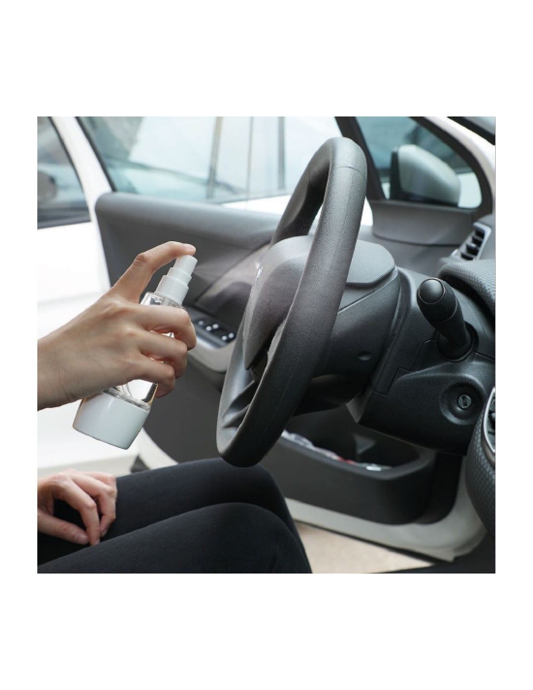 Hand sprüht Flüssigkeit in einem Auto auf das Lenkrad. Sprühgerät ist transparent und weiß.